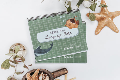 Green spiral-bound book titled 'Level One Language Arts' on a white surface with decorative elements.